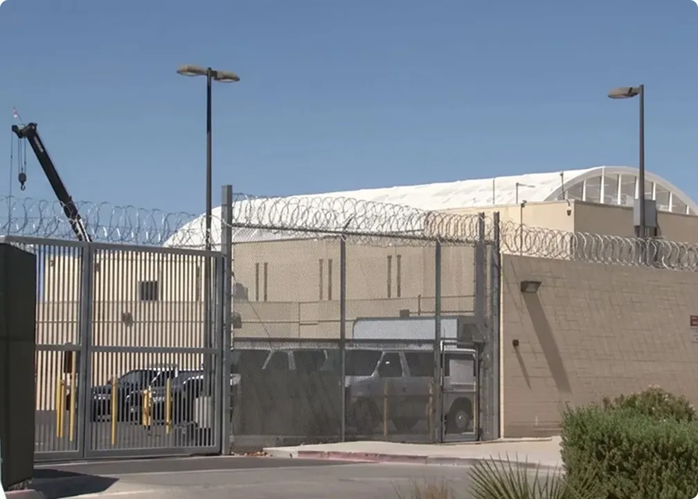 Exterior view of a secure facility with high fences topped with barbed wire and surveillance equipment under a clear blue sky.