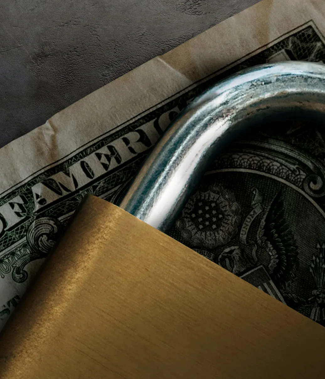 Close-up of a brass padlock securing a U.S. dollar bill under its shackle.