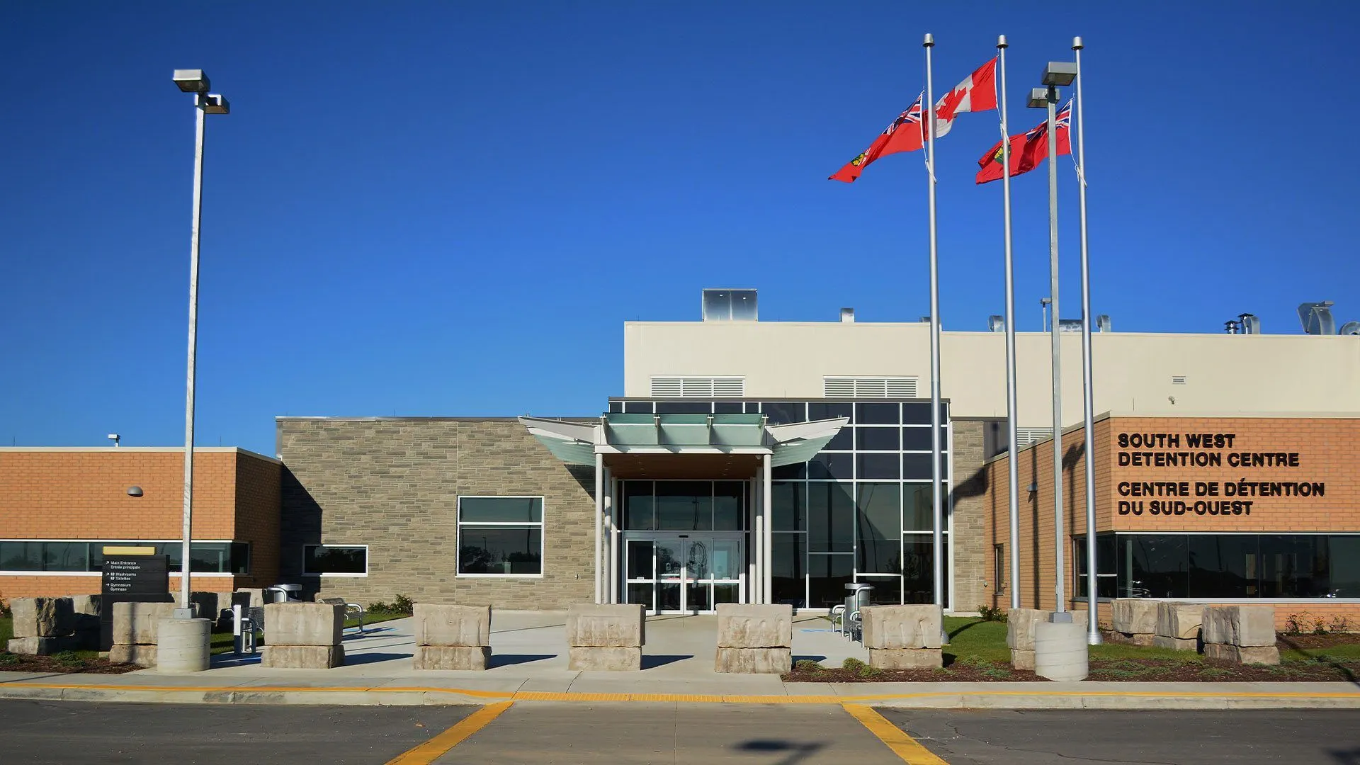 Exterior of South West Detention Centre building with flags flying on poles in front under clear blue sky.