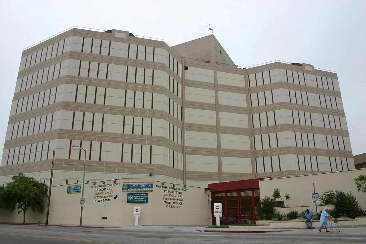 Exterior view of Twin Towers Correctional Facility building with signage and people walking nearby.