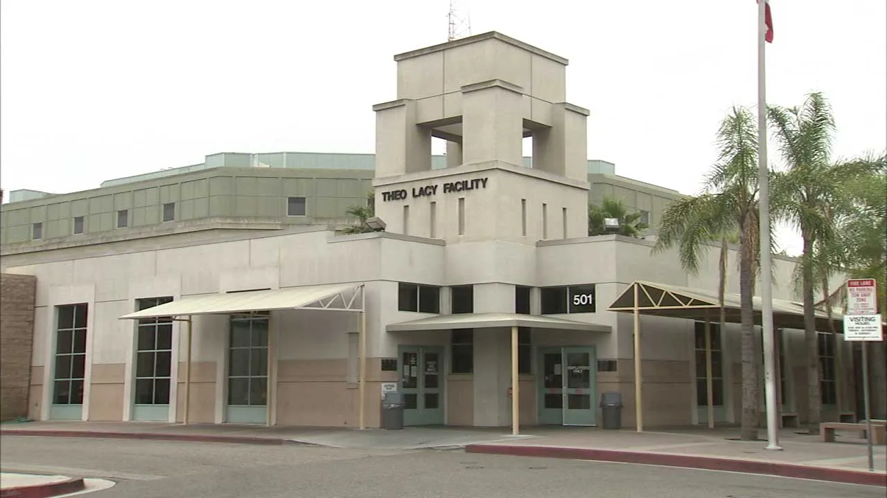 Exterior view of the Theo Lacy Facility building with beige walls, entrance doors, and palm trees nearby.