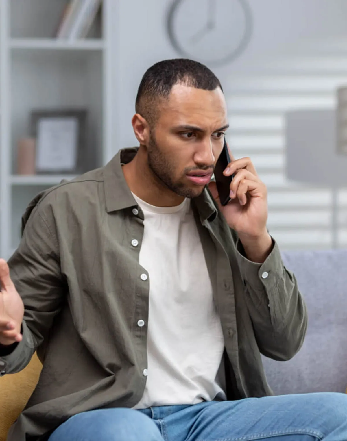 Concerned man sitting on a couch talking on a smartphone with a puzzled expression.