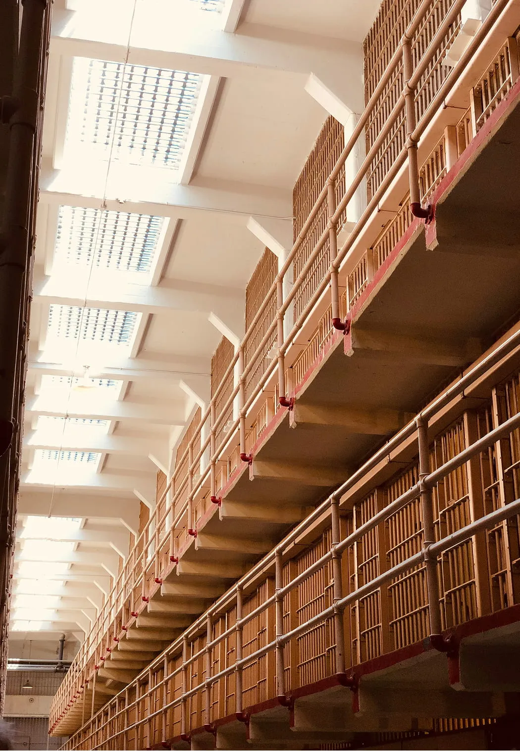 Interior view of a prison cell block with multiple rows of barred cells and bright overhead skylights.