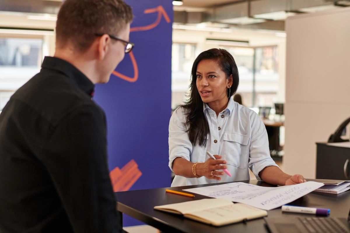 Two apprentices talk while looking at a piece of paper