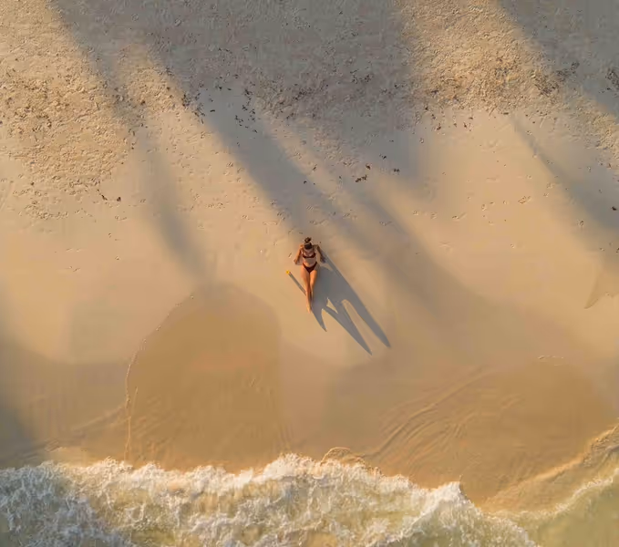 Aerial view of a woman relaxing on the pristine white sand of the private beach at La Valise San Miguel Hotel.