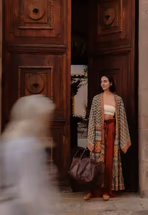 Una mujer elegante con un colorido kimono de pie ante las grandiosas puertas de madera tallada del hotel La Valise San Miguel.
