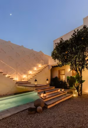 Vista nocturna del patio del hotel La Valise San Miguel con una piscina resplandeciente, escaleras iluminadas con faroles y un ambiente sereno bajo un cielo estrellado.
