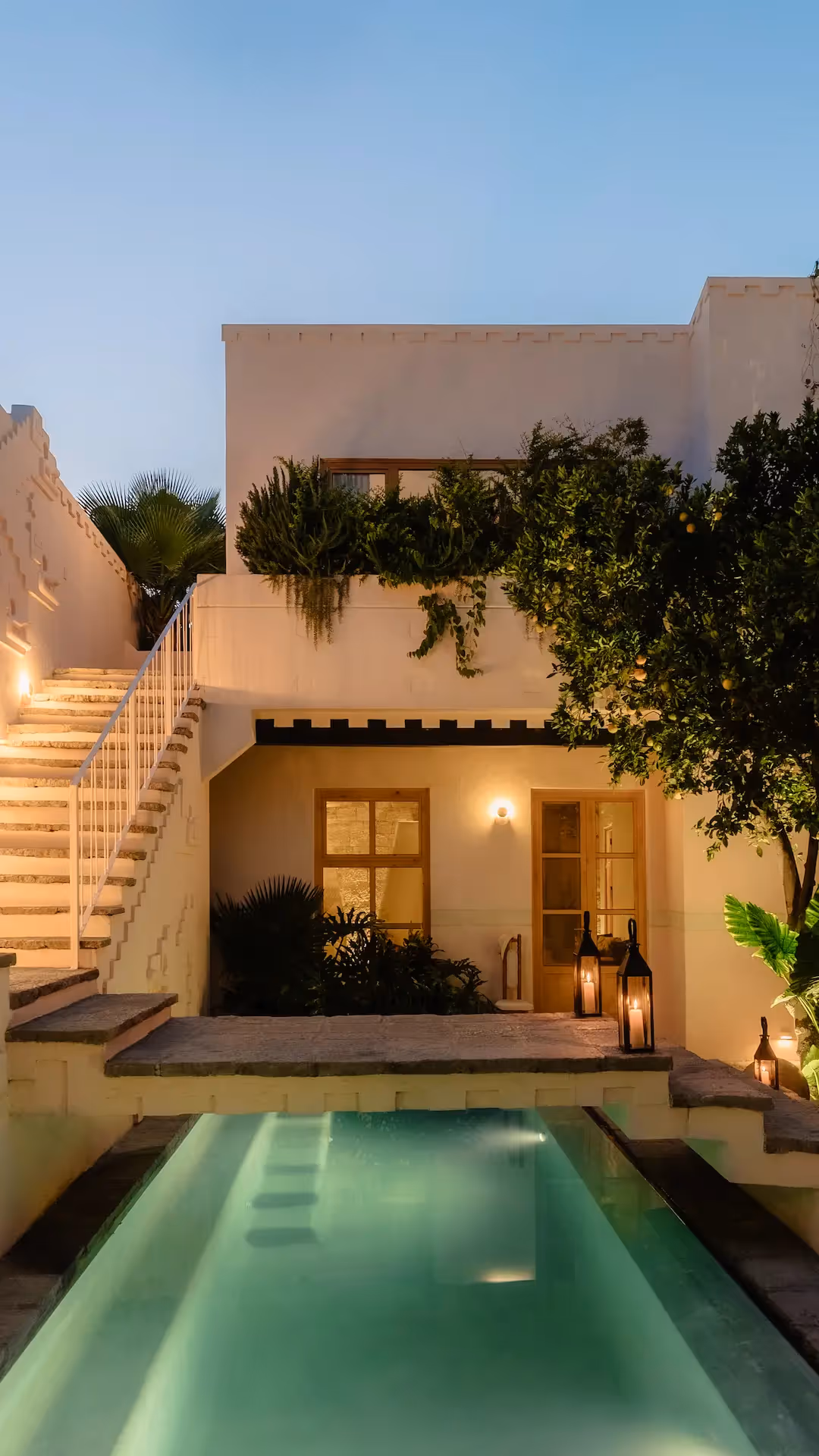 El lujoso patio del hotel La Valise San Miguel cuenta con una piscina iluminada, una escultural escalera blanca y un exuberante jardín al anochecer.