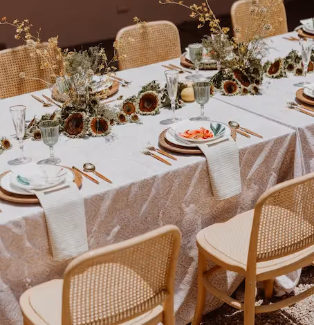 Primer plano de una elegante mesa de comedor con sillas de ratán, manteles de lino y centros de mesa florales en el restaurante del hotel La Valise San Miguel.