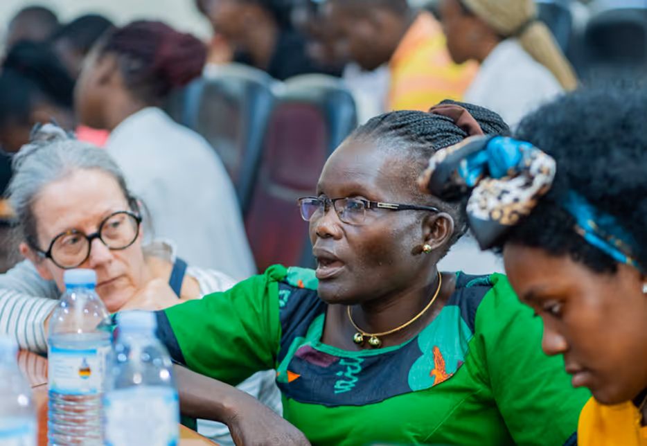 Three women seated closely, engaged in a discussion, with water bottles in the foreground.