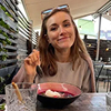 Vrouw die buiten lacht en een kom met eten eet bij een houten tafel.