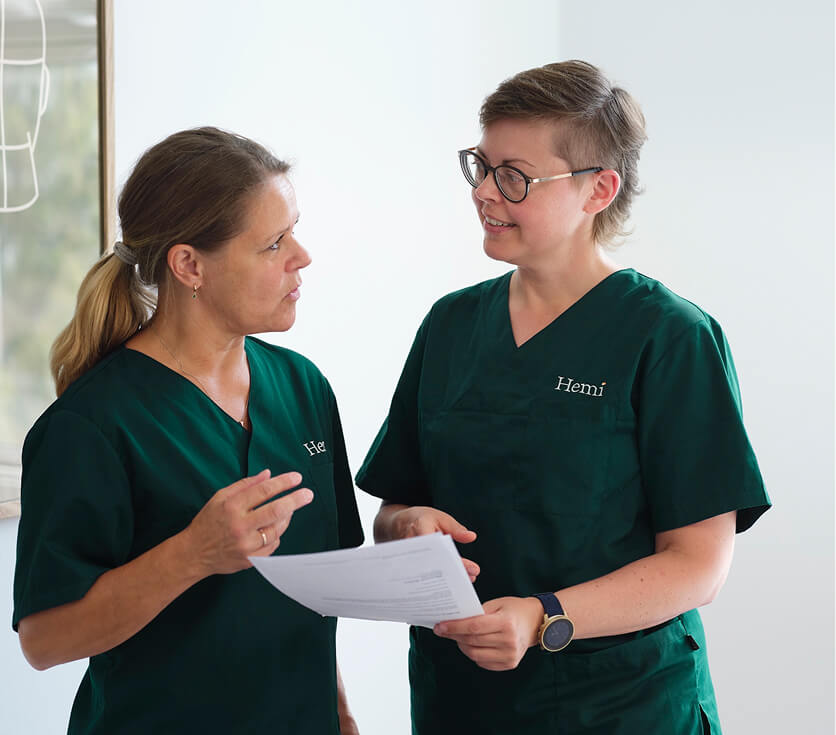 Twee vrouwelijke zorgverleners in groene uniformen die over documenten praten in een lichte kamer.