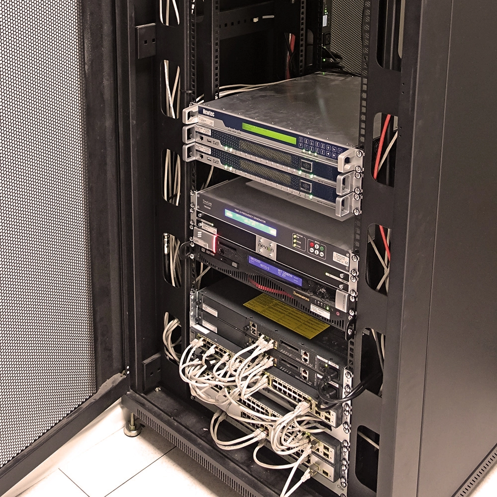 Open server rack with multiple network and audio equipment units wired with white Ethernet and power cables.