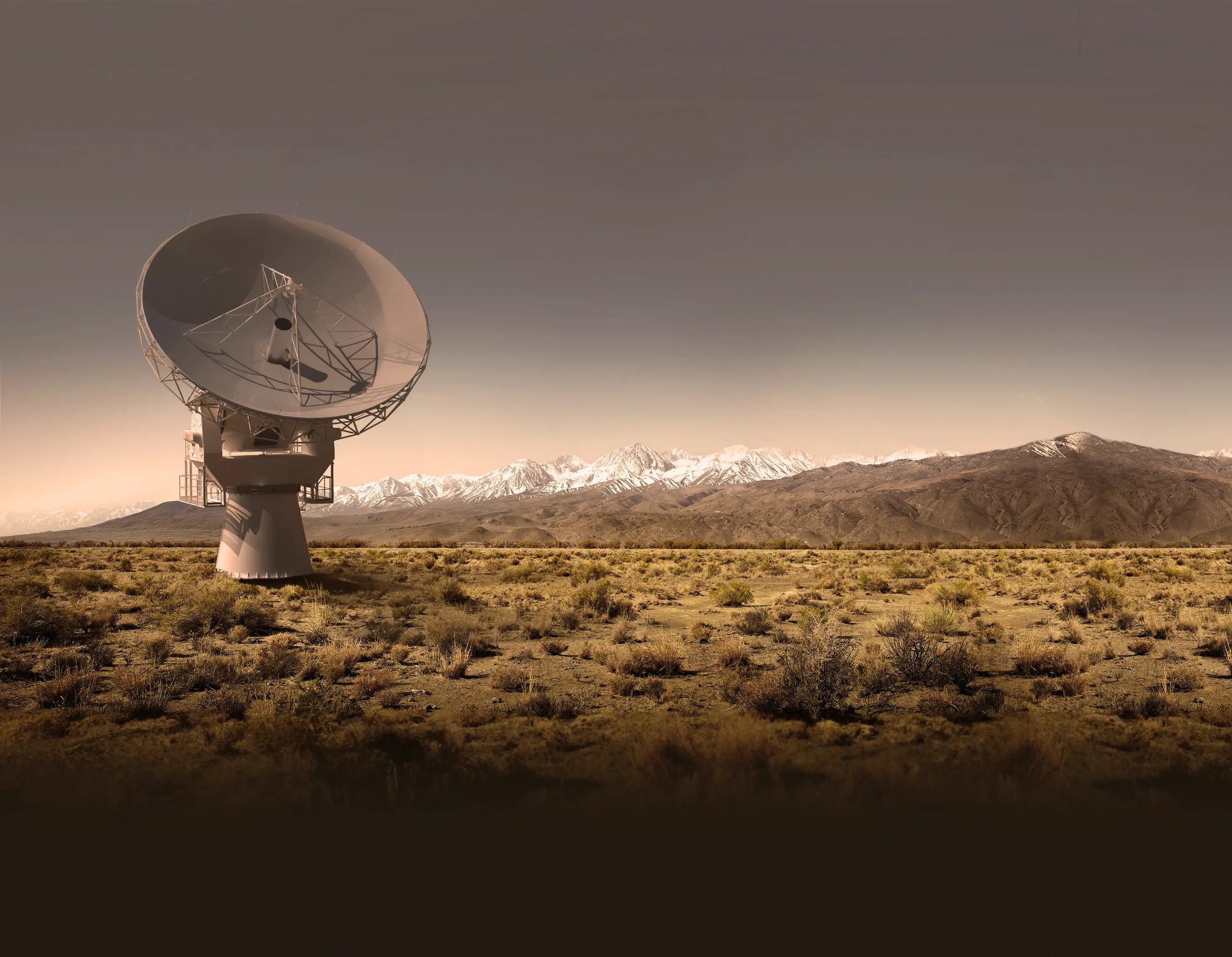 Large satellite dish antenna standing in a dry, shrub-filled plain with a mountain range in the background under a clear sky.