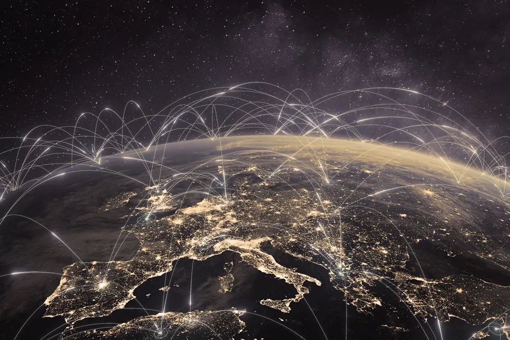 Satellite view of Europe at night showing illuminated cities with light trails representing global communication or data connections across the continent and beyond.