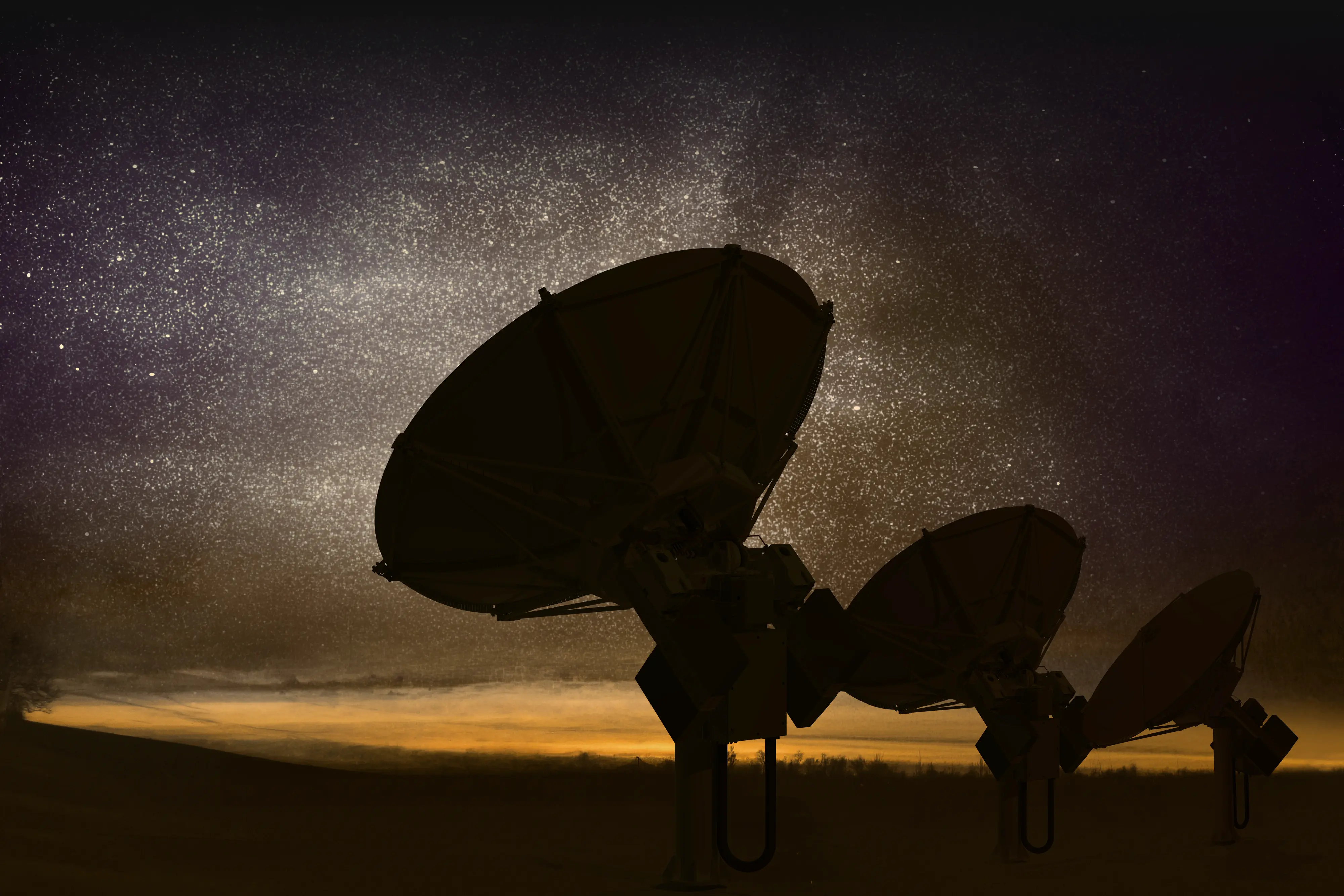 Three large satellite dishes silhouetted against a star-filled night sky with a glowing horizon.