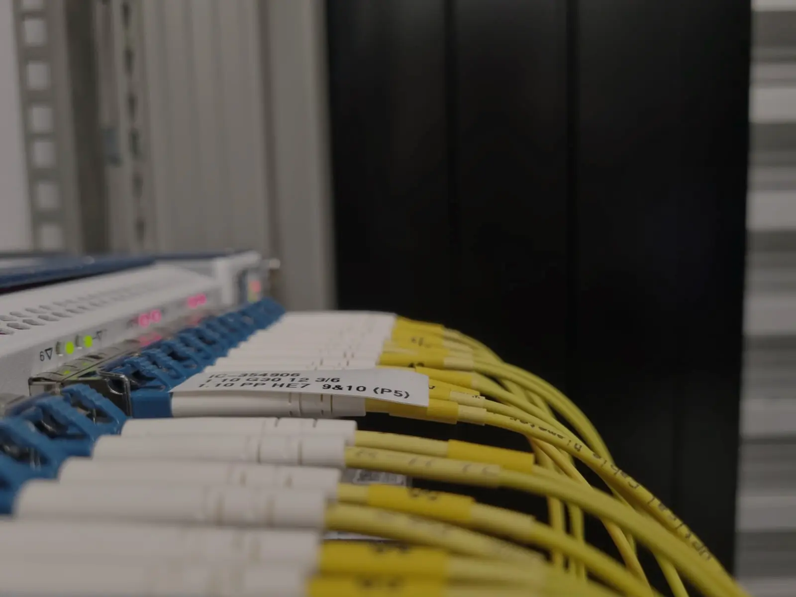 Close-up of multiple yellow and white fiber optic cables connected to a patch panel with blue ports and a white label attached.