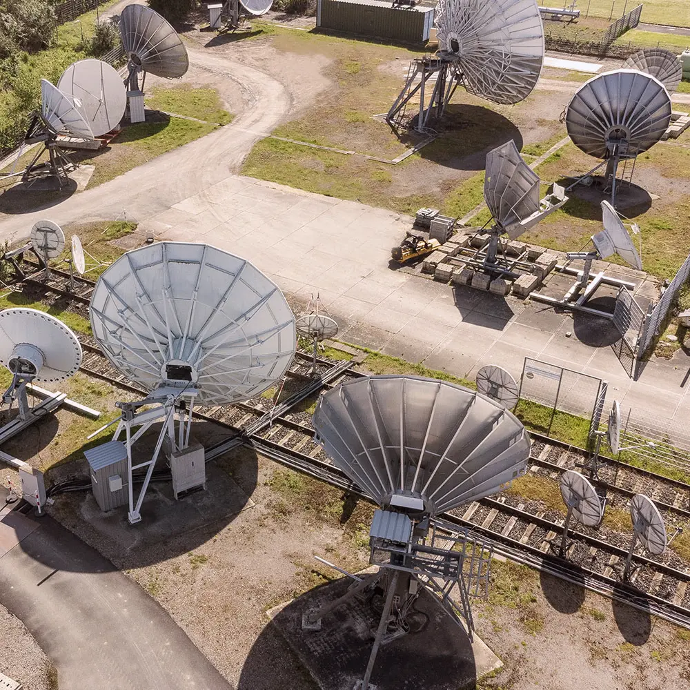 Aerial view of multiple large satellite dishes and antennas at a communication facility with grassy areas and paved paths.