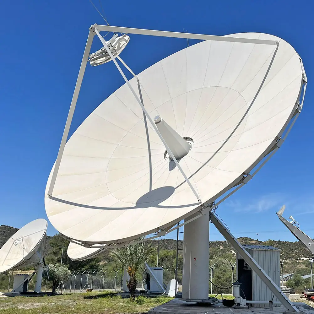 Large white satellite dishes positioned outdoors under a clear blue sky with green hills and trees in the background.