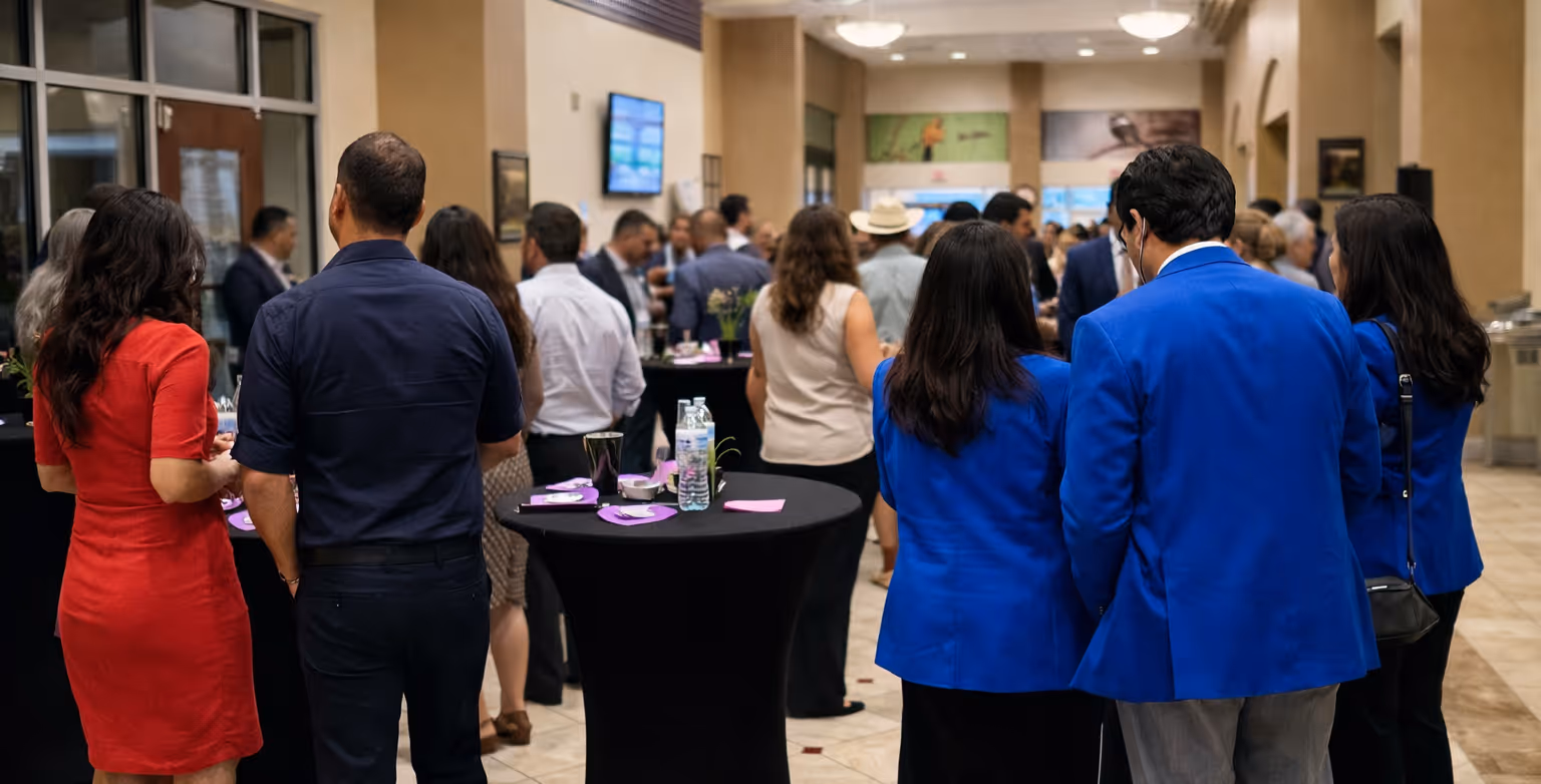 People dressed in business attire socializing at a networking event in a spacious indoor venue with cocktail tables.