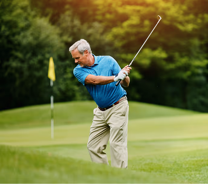 Middle-aged man in a blue polo shirt swinging a golf club on a green golf course near a flag.