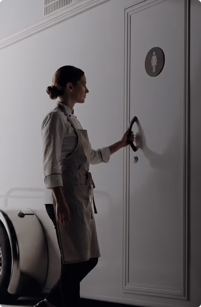 Woman in apron opening door with female restroom sign