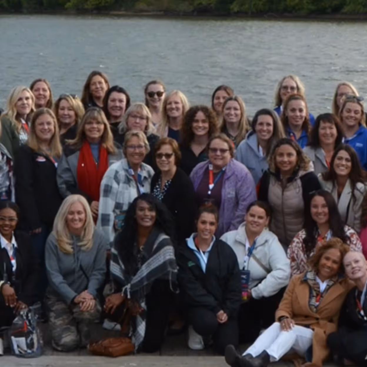 Large group of women gathered outdoors by a body of water