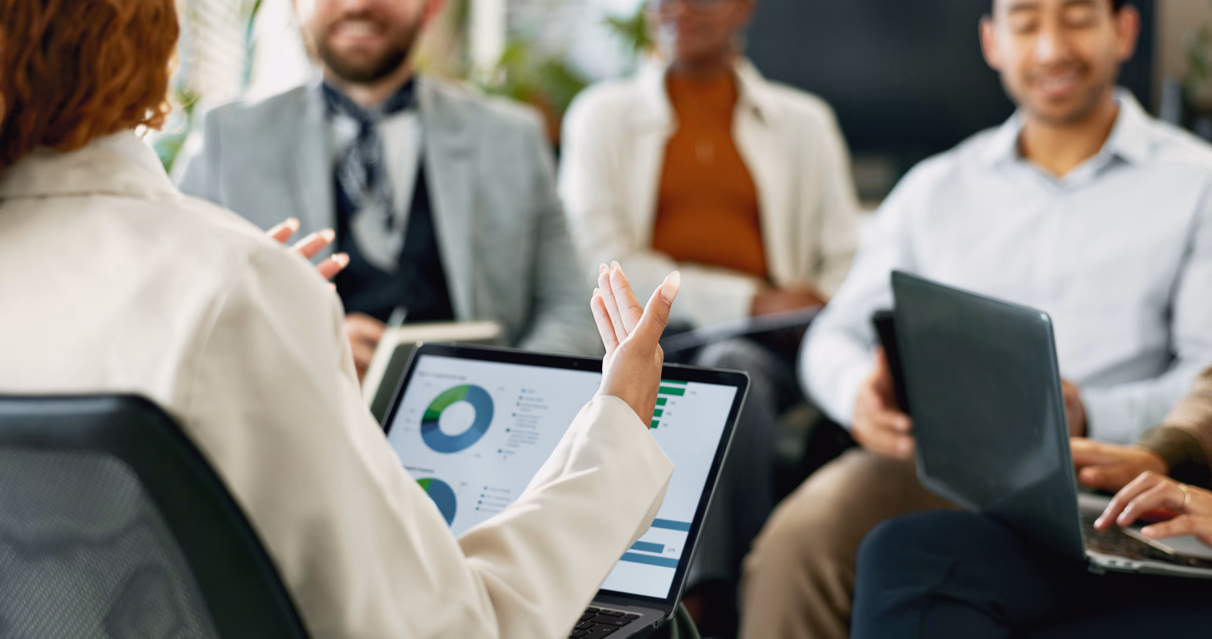 Business meeting with diverse group discussing data charts on laptop screens