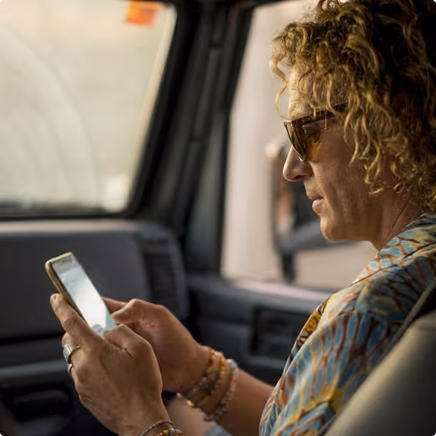 Person with curly hair and sunglasses using smartphone inside vehicle