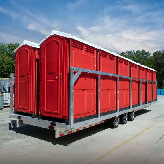 Trailer carrying multiple red portable restrooms outdoors on concrete surface