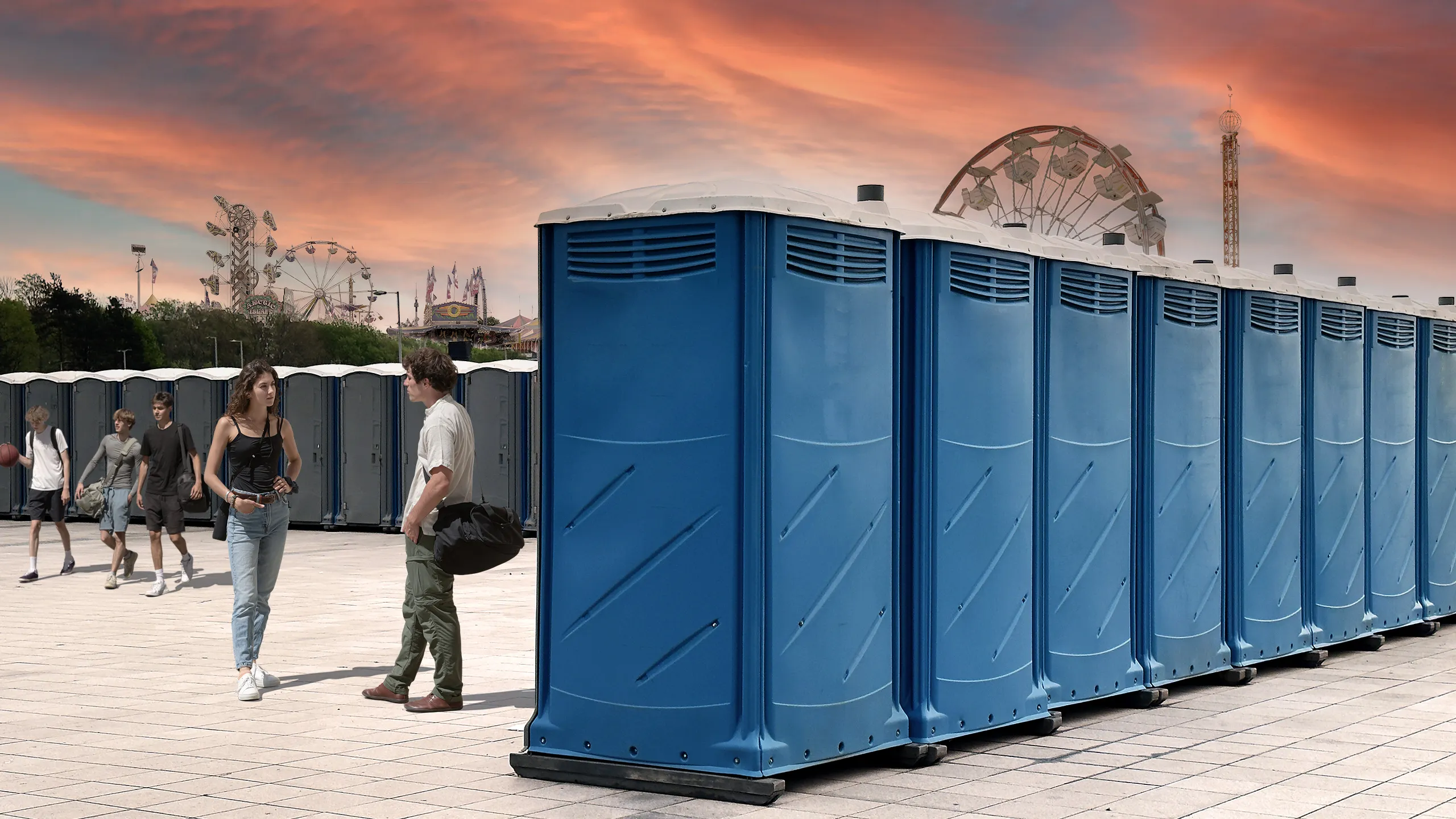 Row of blue portable restrooms at an outdoor event with people and amusement park rides in the background