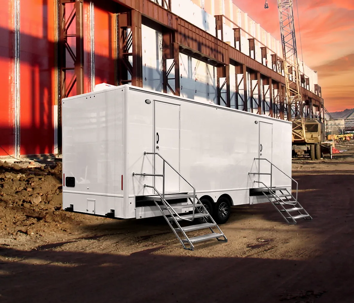 White restroom trailer with two entry stairs parked at construction site during sunset