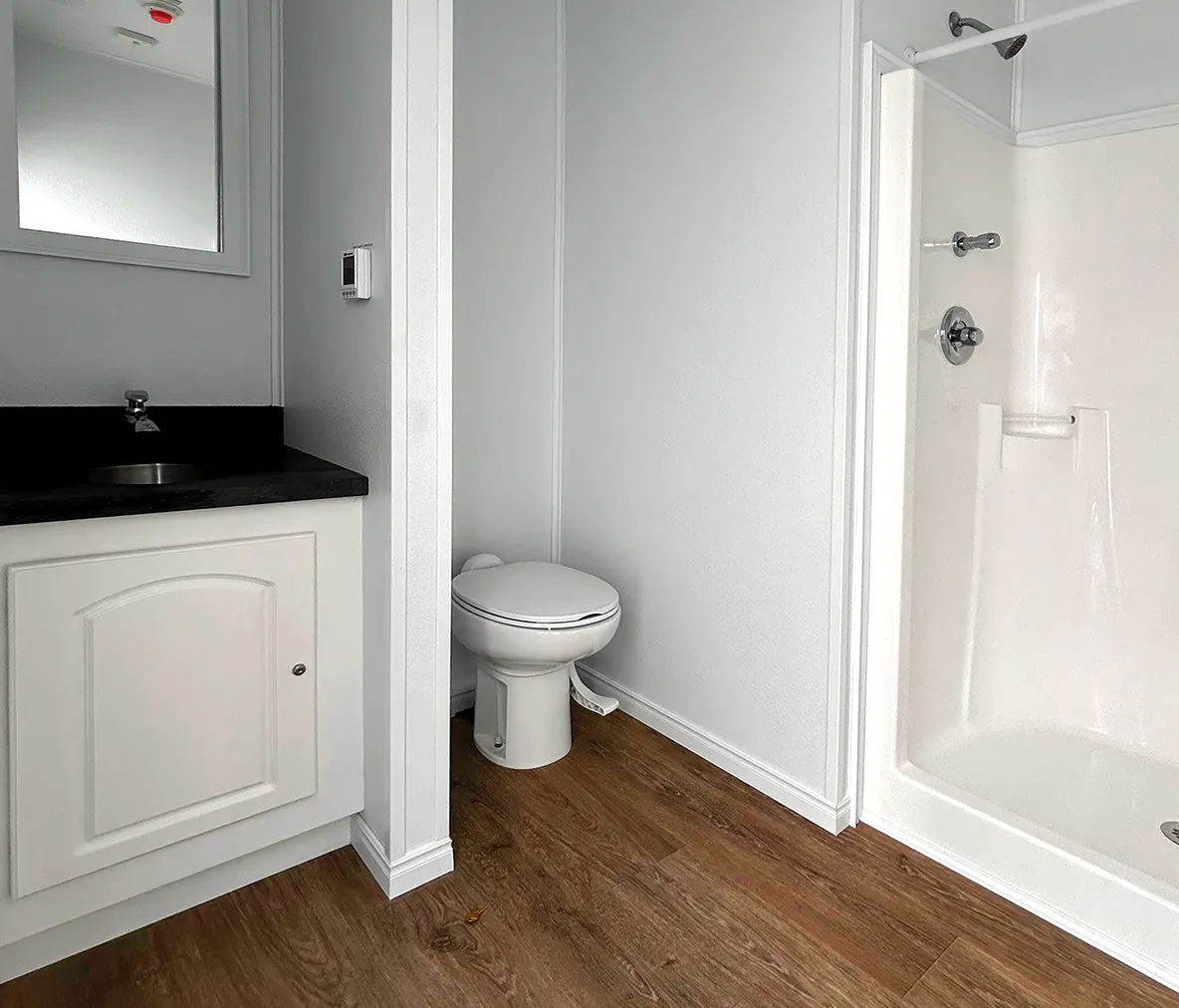 Construction accommodation bathroom interior with white toilet, shower, and sink with black countertop