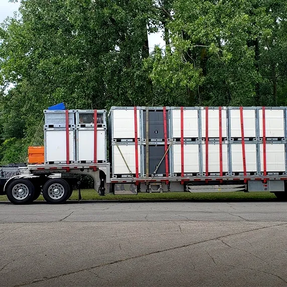 Flatbed trailer loaded with multiple stacked white storage containers secured with red straps outdoors