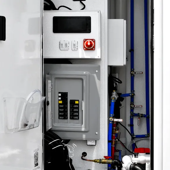 Open electrical control panel with circuit breakers and blue piping inside portable restroom trailer interior