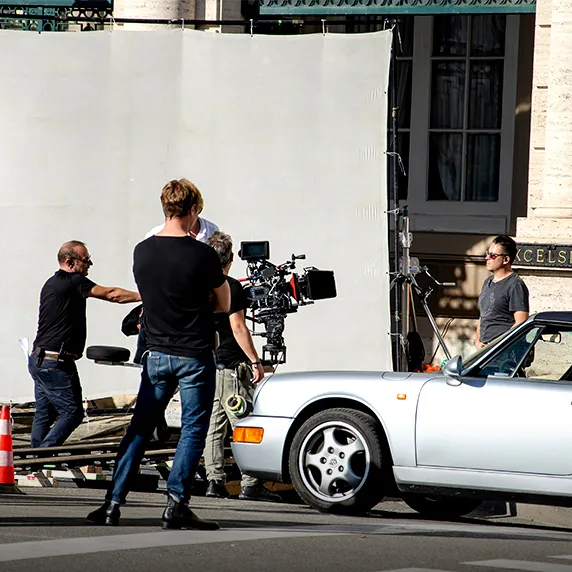 Film crew setting up camera equipment near silver sports car on street