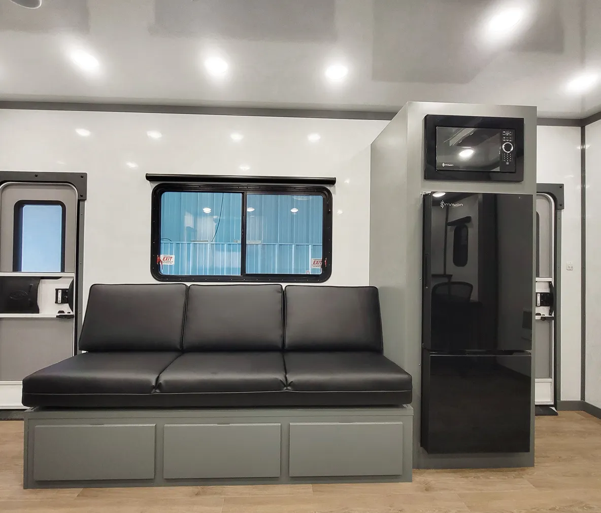 Black cushioned bench seat with gray storage base next to black microwave and refrigerator inside a mobile unit interior