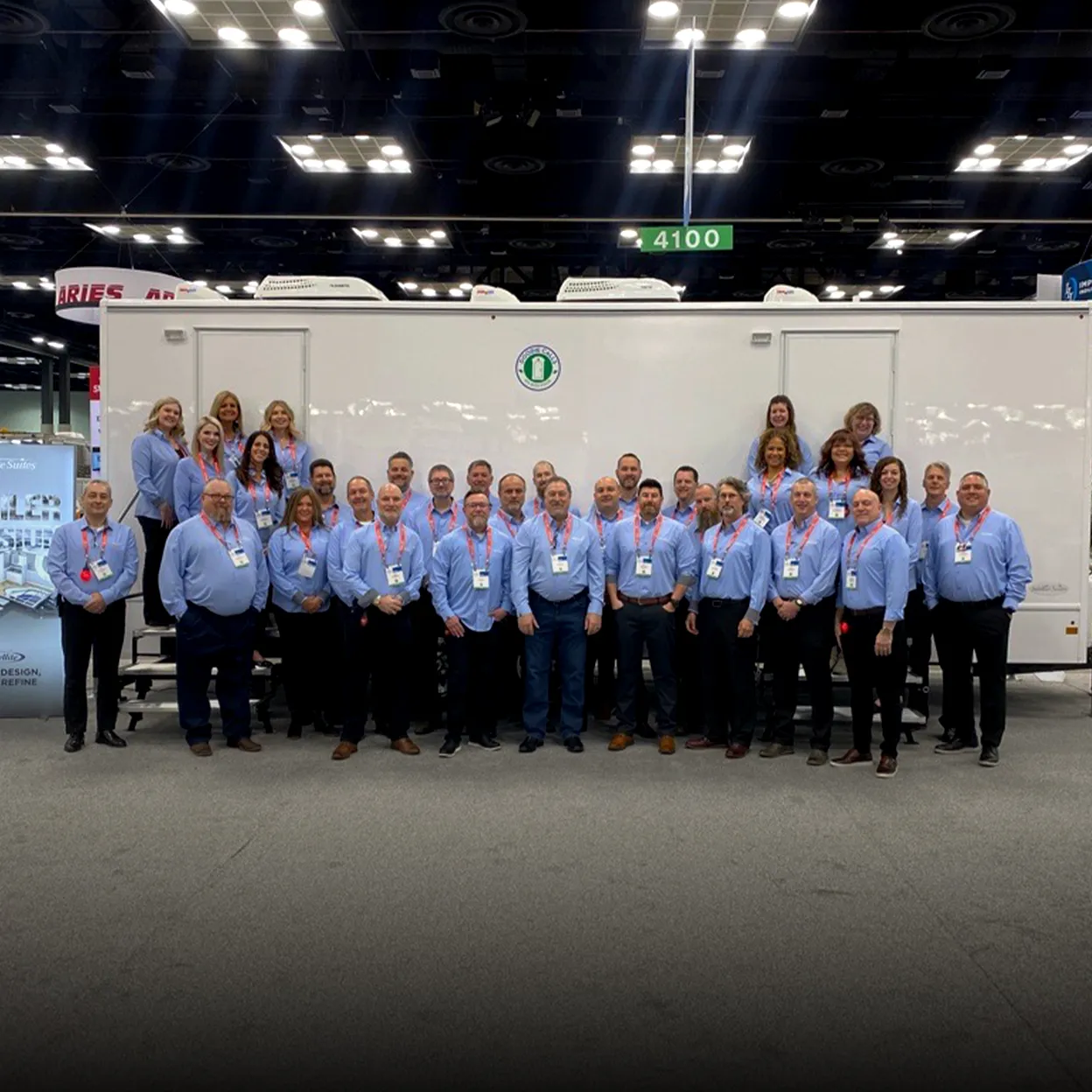 Group of people in blue shirts with red lanyards standing in front of a white trailer at tradeshow