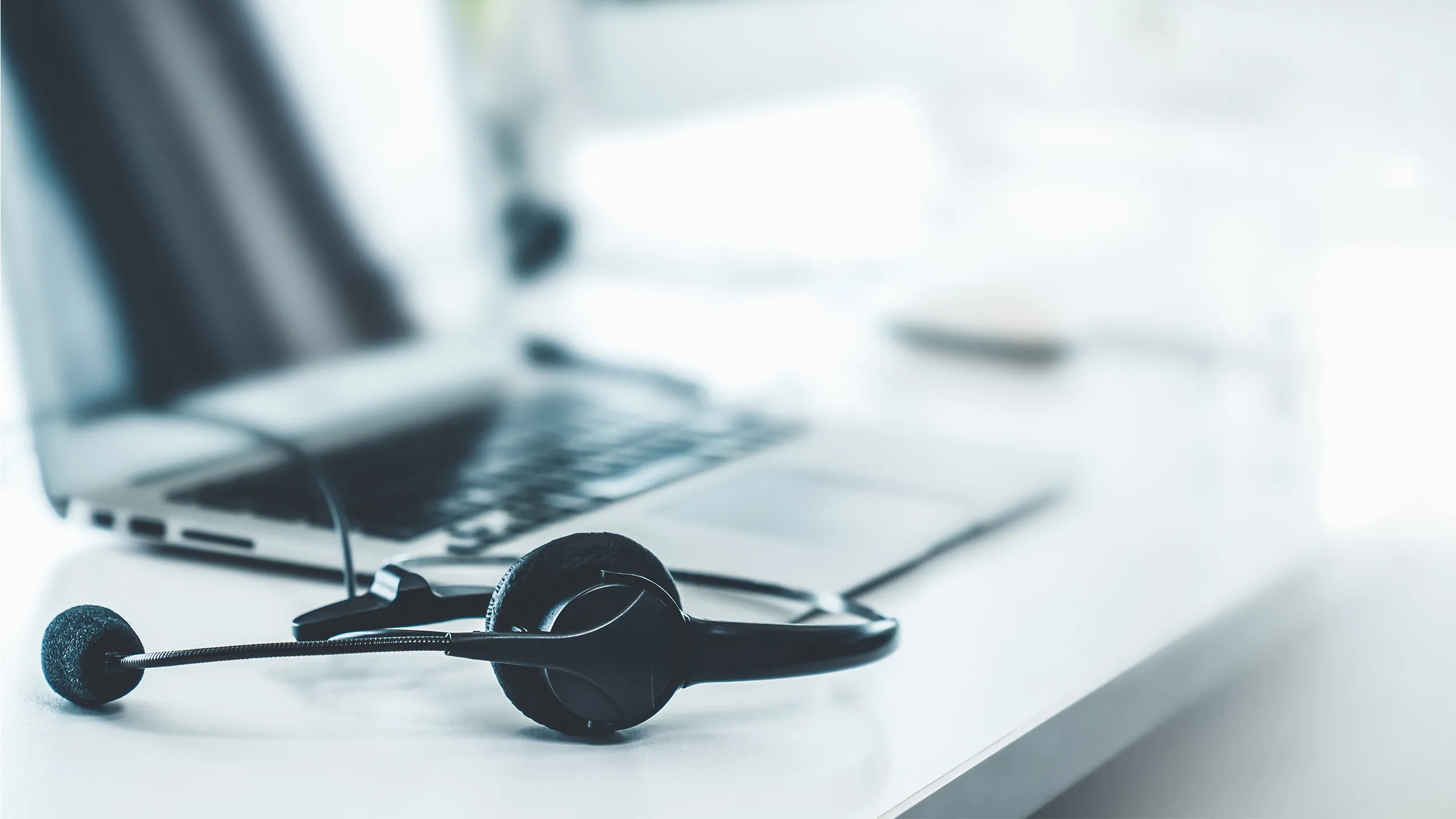Black headset with microphone resting on a white desk in front of a laptop keyboard