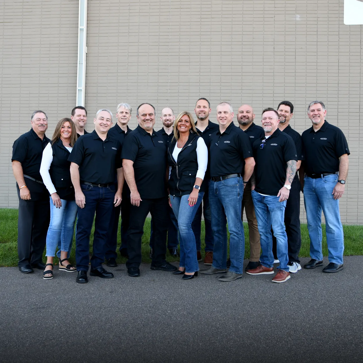 Group of training experts in black Satellite Industries shirts standing outdoors against a tan brick wall