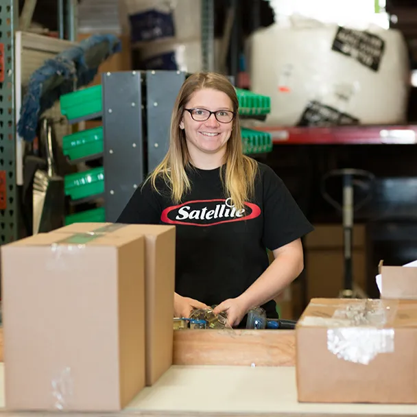 Woman in black Satellite Industries t-shirt assembling or packing items at workbench in warehouse