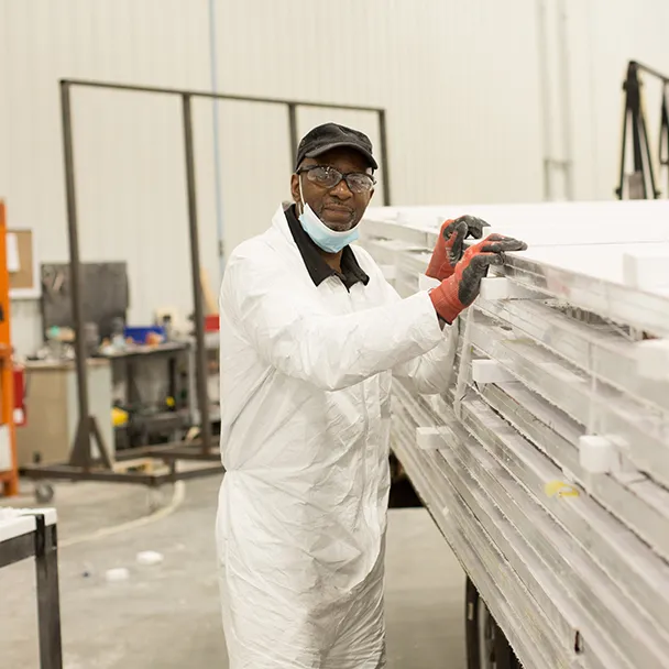 Worker in white protective coverall and gloves handling stacked panels in industrial setting