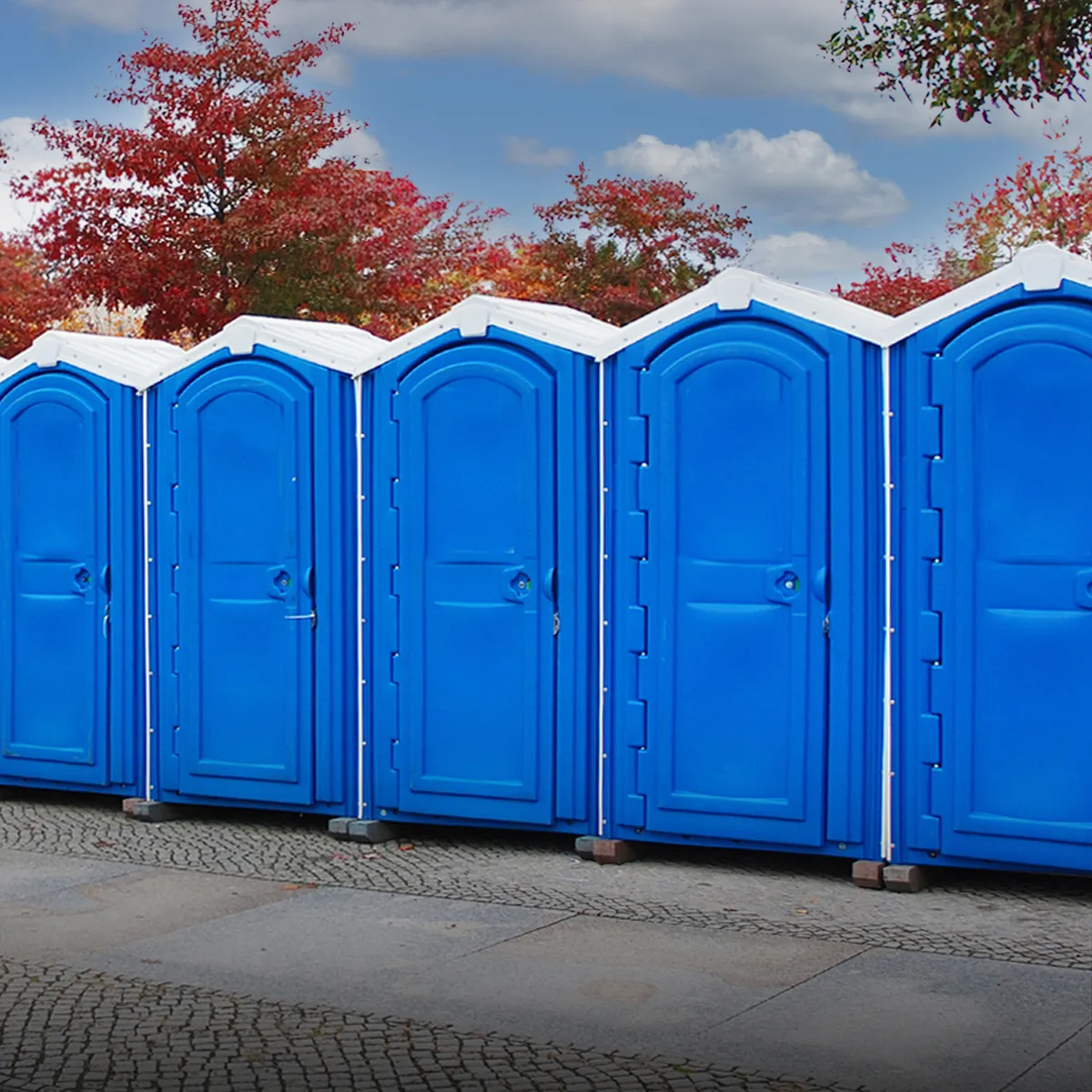 Row of blue portable restrooms with white roofs outdoors near autumn trees