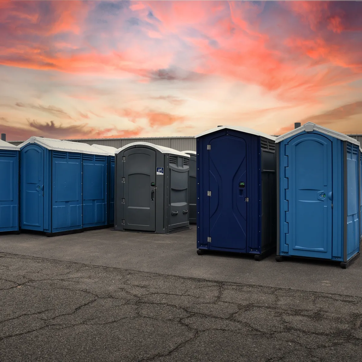 Group of blue and gray portable restrooms outdoors at sunset