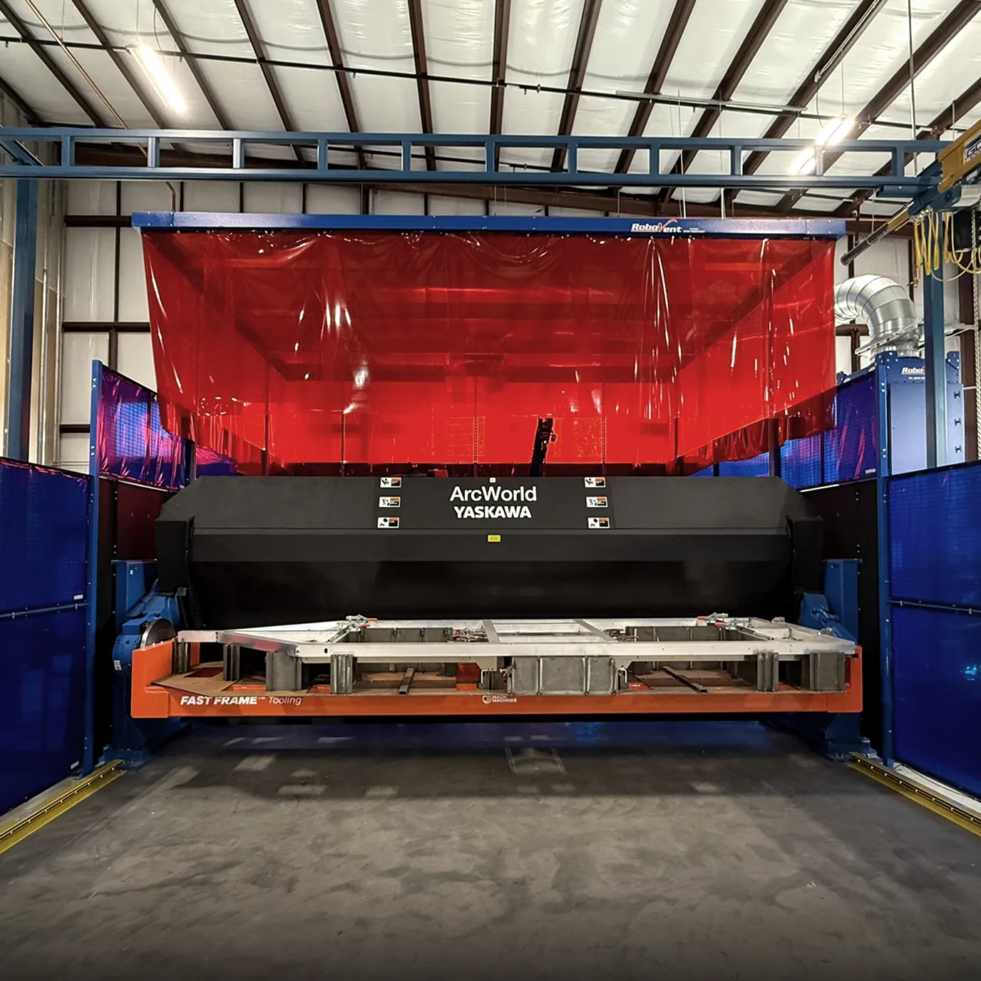Industrial welding machine with ArcWorld Yaskawa branding inside a workshop with red safety curtain