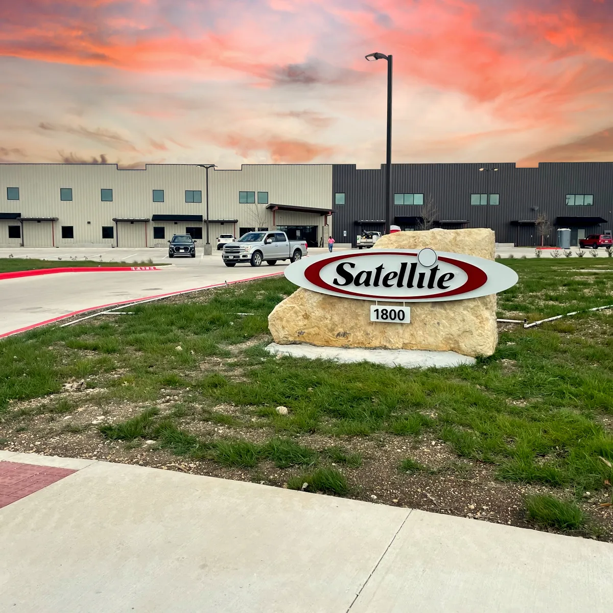 Satellite Industries stone sign with logo in front of industrial building at sunset