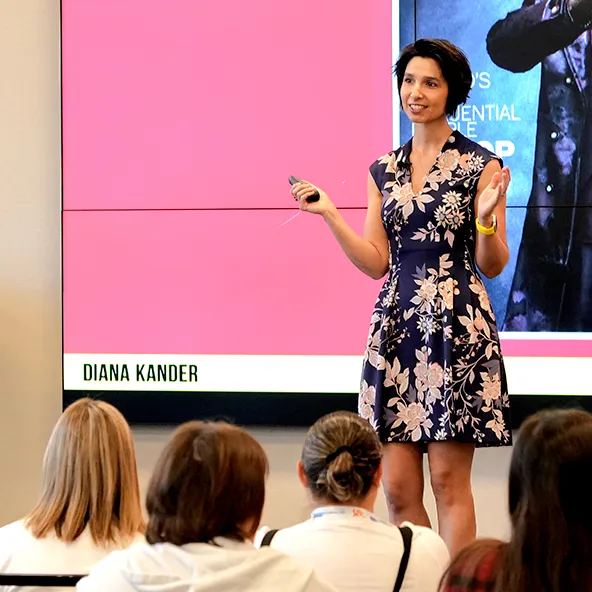 Woman in floral dress giving presentation to seated audience