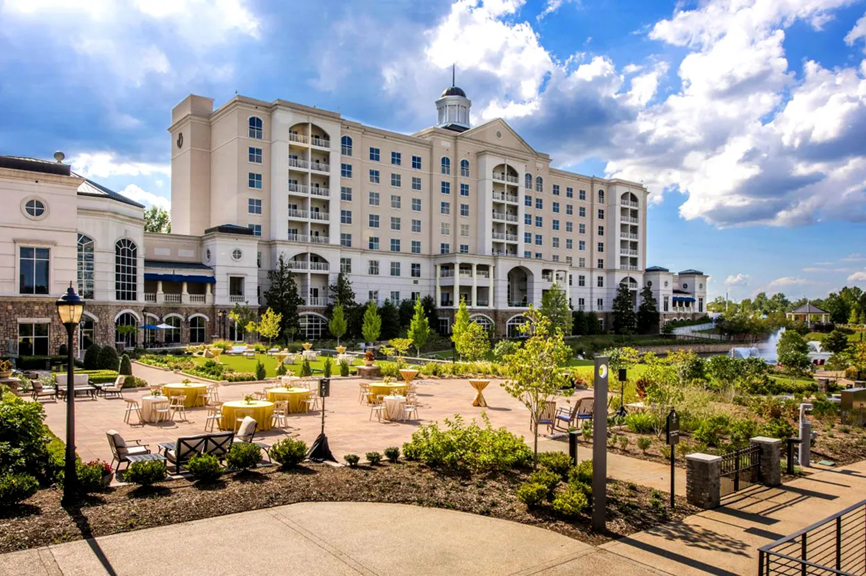 Large beige multi-story hotel building with balconies and outdoor patio seating area under a partly cloudy sky