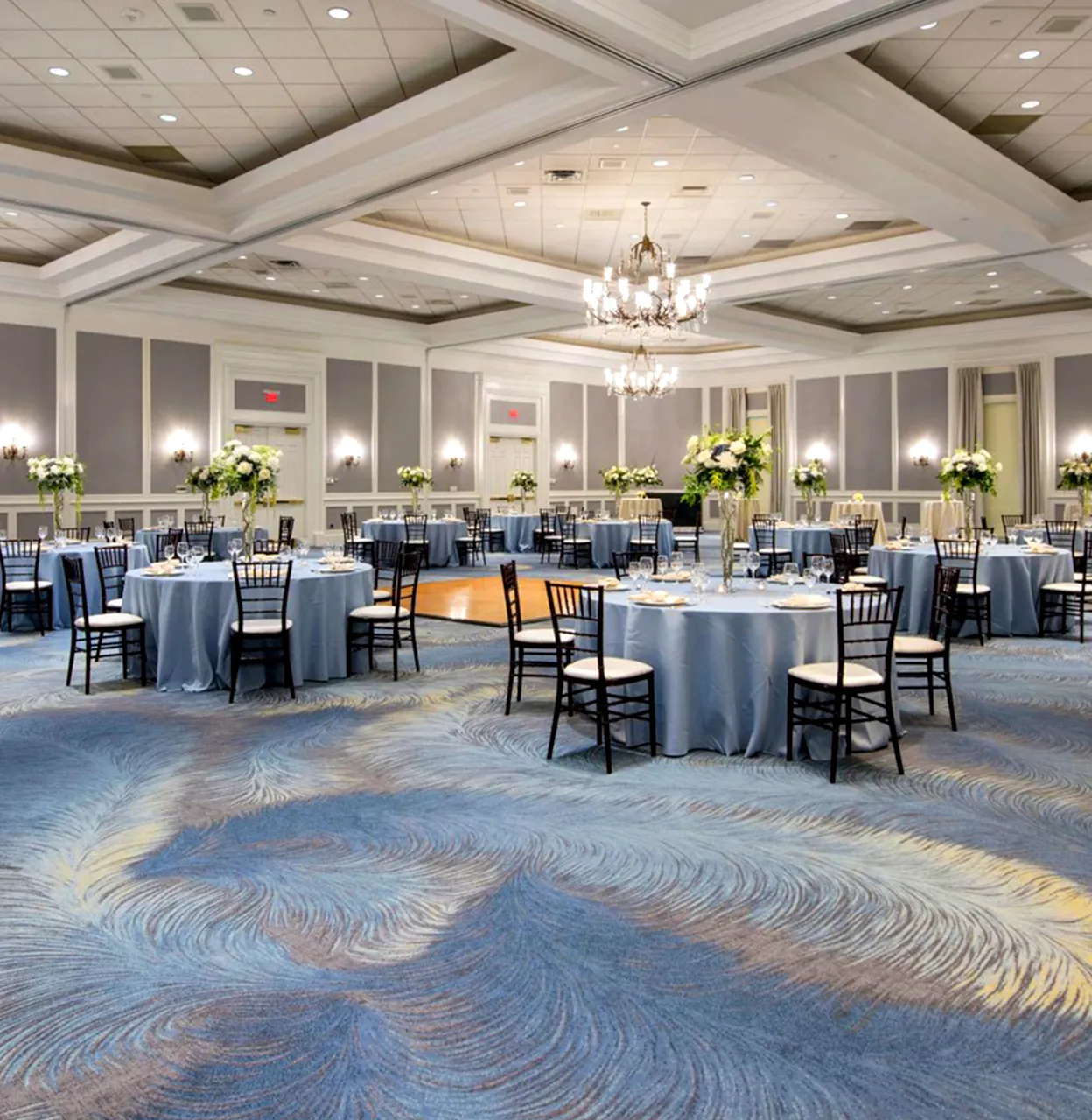 Hotel banquet room with round tables covered in blue tablecloths and black chairs