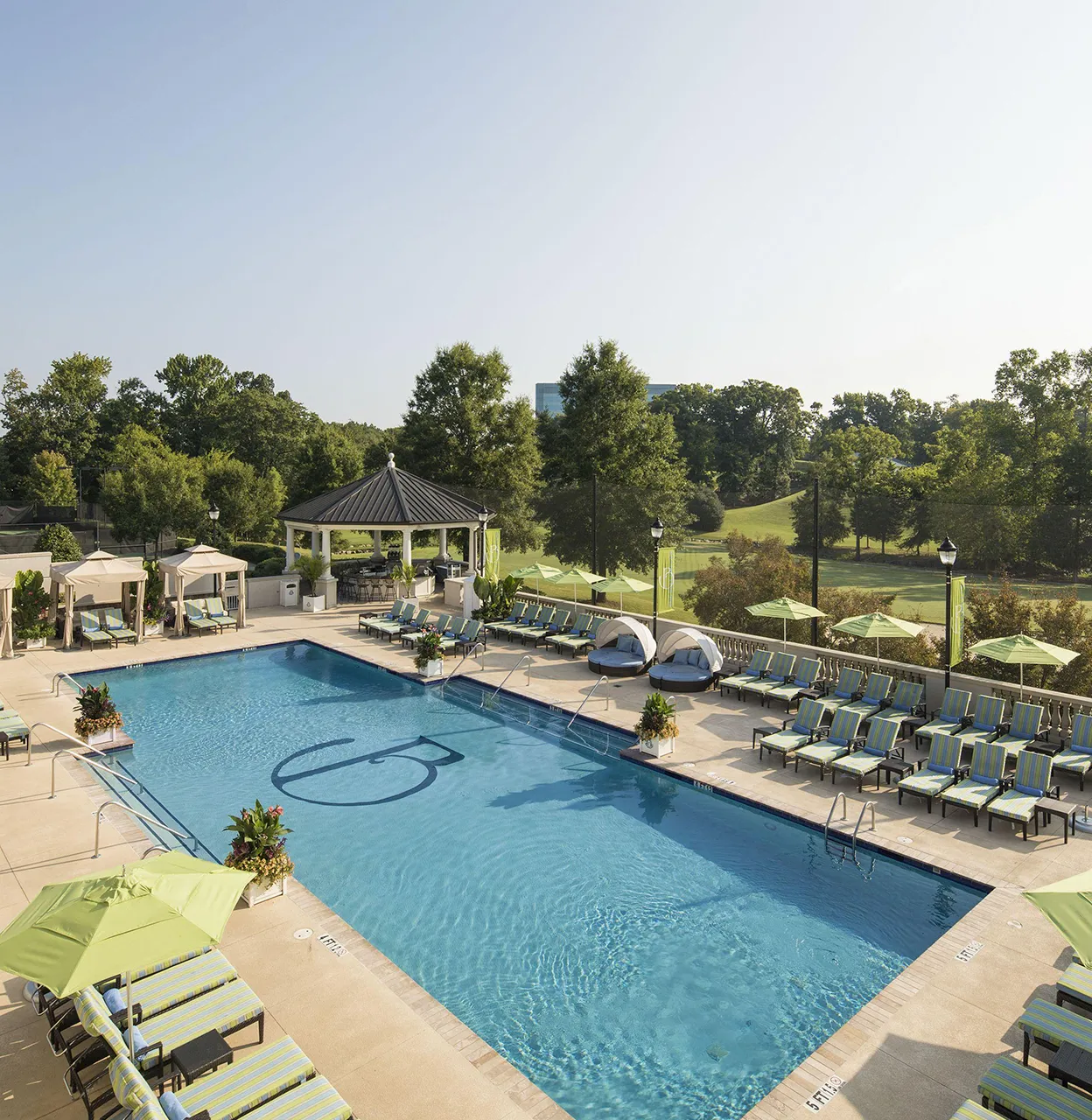 Outdoor swimming pool with green-striped lounge chairs and green umbrellas surrounding it
